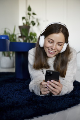 Frau mit Kopfhörern schaut lächelnd aufs Handy