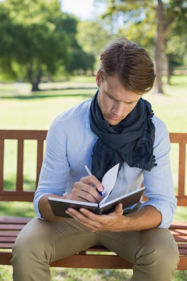 Mann sitzt auf der Parkbank und blättert im Notizbuch