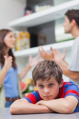 Trauriger Junge mit streitenden Eltern im Hintergrund