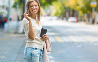 Ältere Frau mit Kaffeebecher steht lächelnd auf der Straße