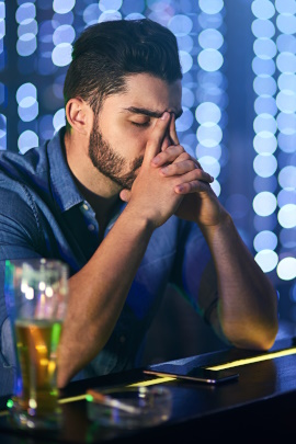 Verzweifelter Mann mit Bierglas sitzt allein an der Theke