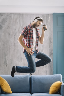 Mann tanzt mit Kopfhörern zu Hause auf dem Sofa