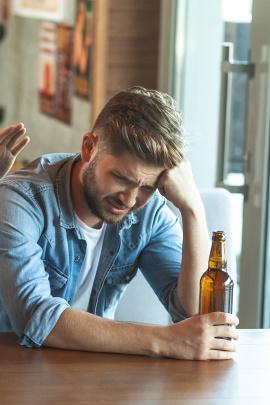 Mann an der Theke schaut unglücklich auf Bierflasche