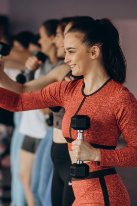 Gruppe junger Menschen schwingt Hanteln im Fitnesskurs