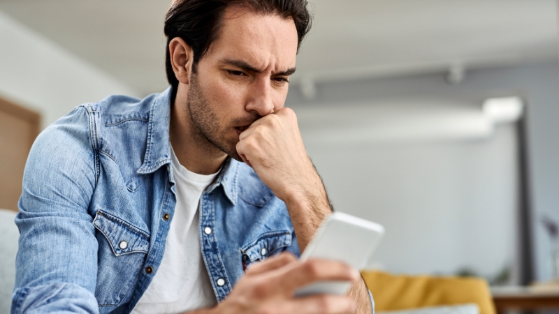 Mann schaut auf sein Handy und fragt sich, ob seine Ex-Freundin noch an ihm interessiert ist