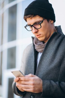 Winterlich gekleideter Mann schaut ernst aufs Handy