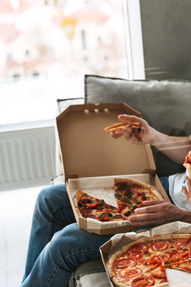 Zwei nicht erkennbare Personen essen Pizza auf dem Sofa