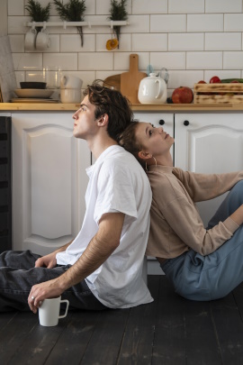 Mann und Frau sitzen mit Rücken zueinander auf dem Küchenboden