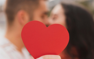 Verliebtes Paar küsst sich und hält rotes Herz in die Kamera