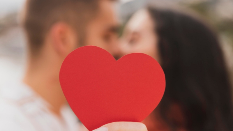 Verliebtes Paar küsst sich und hält rotes Herz in die Kamera