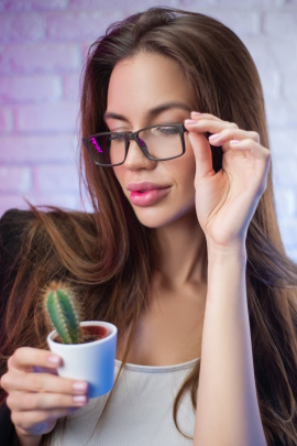 Frau betrachtet einen kleinen Kaktus durch ihre Brille