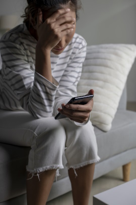 Frau mit Handy sitzt genervt auf dem Bett