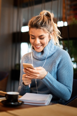 Frau sitzt im Café und schaut lächelnd aufs Handy