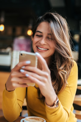 Frau im Café schaut lächelnd aufs Handy