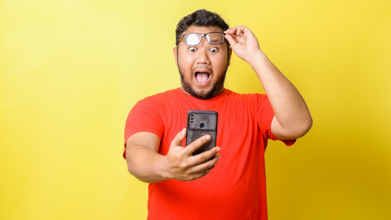 Mann hält Brille und blickt schockiert aufs Handy