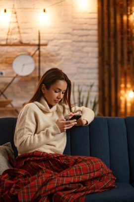 Frau sitzt zu Hause auf dem Sofa und schaut aufs Handy