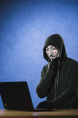 Hacker mit Maske sitzt nachdenklich vorm Laptop