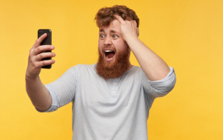 Mann mit langem Bart schaut erschrocken aufs Handy