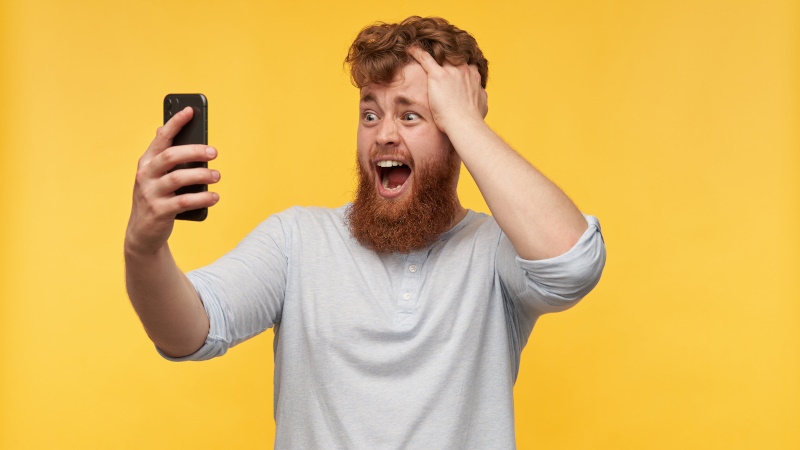 Mann mit langem Bart schaut erschrocken aufs Handy