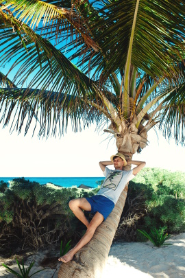 Mann lehnt sich gegen Palme am Strand und entspannt