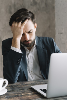 Mann sitzt grübelnd vorm Laptop am Schreibtisch