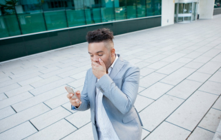 Mann vor Bürogebäude schaut schockiert aufs Handy