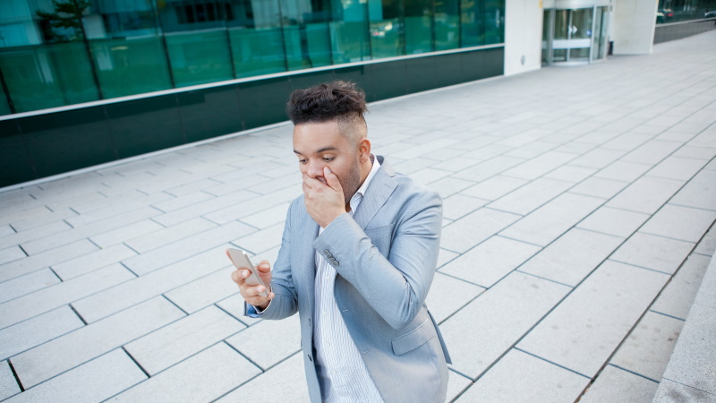 Mann vor Bürogebäude schaut schockiert aufs Handy