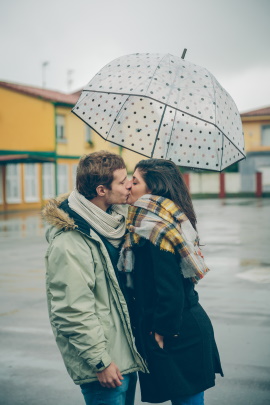Paar küssend bei schlechtem Wetter unterm Schirm