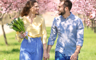 Mann und Frau laufen Händchen haltend durch blühenden Park