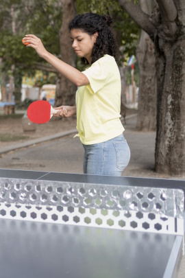 Frau macht Aufschlag beim Tischtennis im Park