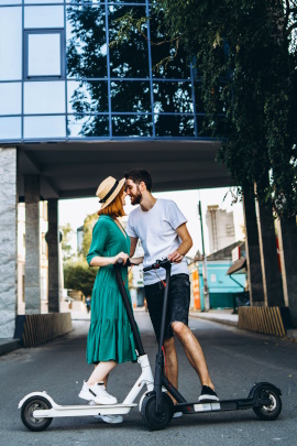 Mann und Frau mit E-Scootern stehen küssend auf der Straße