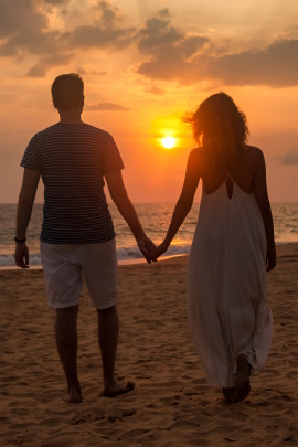 Paar läuft Händchen haltend bei Sonnenuntergang am Strand entlang
