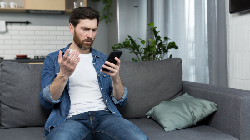 Mann auf der Couch schaut verwirrt aufs Handy