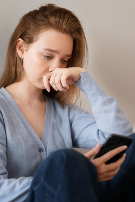 Frau schaut traurig auf ihr Handy, weil ihr Schwarm den Kontakt abgebrochen hat