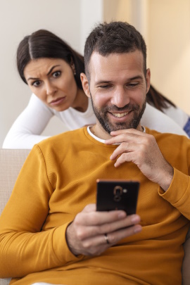 Frau beobachtet eifersüchtig ihren Partner beim Schreiben am Handy