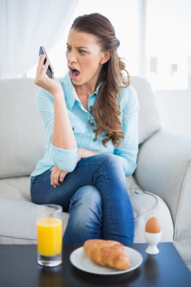 Frau beim Frühstück schaut verärgert auf ihr Smartphone