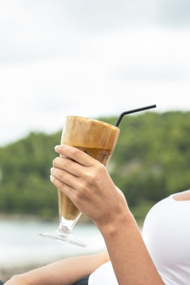 Frauenhand hält Kaffee-Getränk vor schöner Landschaft