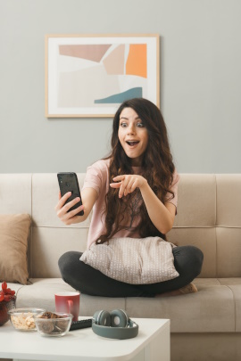 Frau sitzt auf dem Sofa und schaut erstaunt aufs Handy