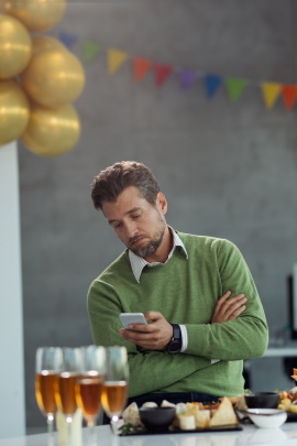 Mann schaut nachdenklich aufs Handy während Geburtstagsparty