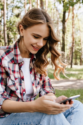 Frau im Park schaut lächelnd aufs Smartphone