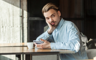 Ex-Freund mit Handy sitzt nachdenklich am Tisch