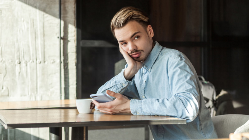 Ex-Freund mit Handy sitzt nachdenklich am Tisch