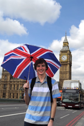 Mann mit Regenschirm steht lächelnd am Big Ben in London