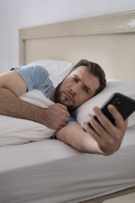 Mann liegt im Bett und schaut verwundert aufs Handy