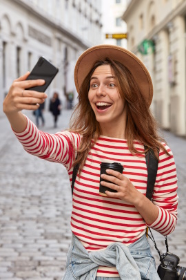 Reisende Frau in der Stadt schaut lachend aufs Handy