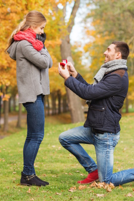 Mann kniet vor Frau im Park und macht Heiratsantrag