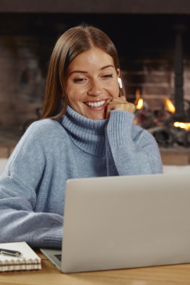 Frau sitzt zuhause lächelnd am Laptop