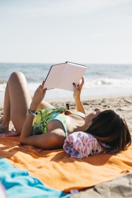 Frau liegt am Strand und liest ein Buch