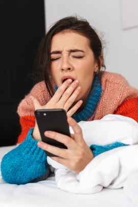 Gähnende Frau mit Smartphone in der Hand