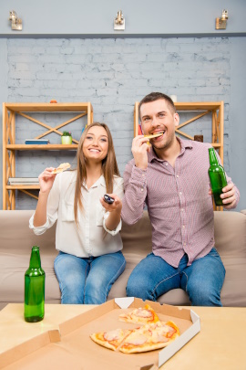 Paar mit Bier und Pizza sitzt lachend vor dem Fernseher